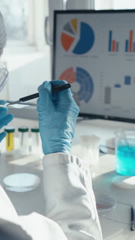 A scientist in a lab coat and gloves conducts vital vaccine research, carefully examining a test tube and analyzing complex data on a monitor, highlighting the importance of their work for healthcare
