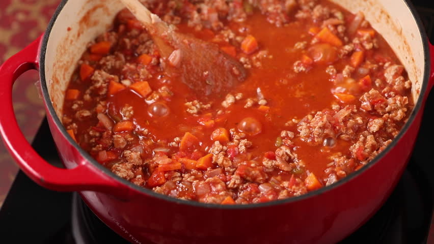 Cooking beef chili, simmering in a pot on a stove, stirring with a wooden spoon