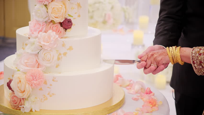 A bride and a groom cutting a wedding cake on the Indian wedding party. Close up shot footage