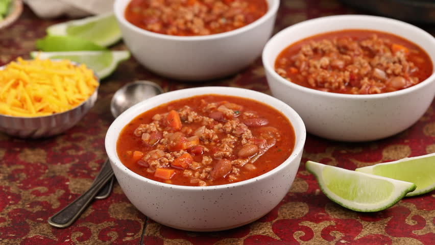 Serving beef chili in bowls, adding grated cheddar cheese on top