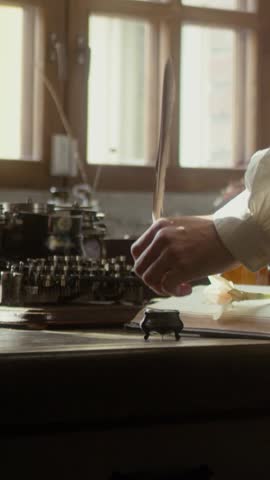 A man writer dips his pen into an inkwell and prepares to write a book in his workshop. Cosplay of the Middle Ages. Cinematic concept. Close-up
