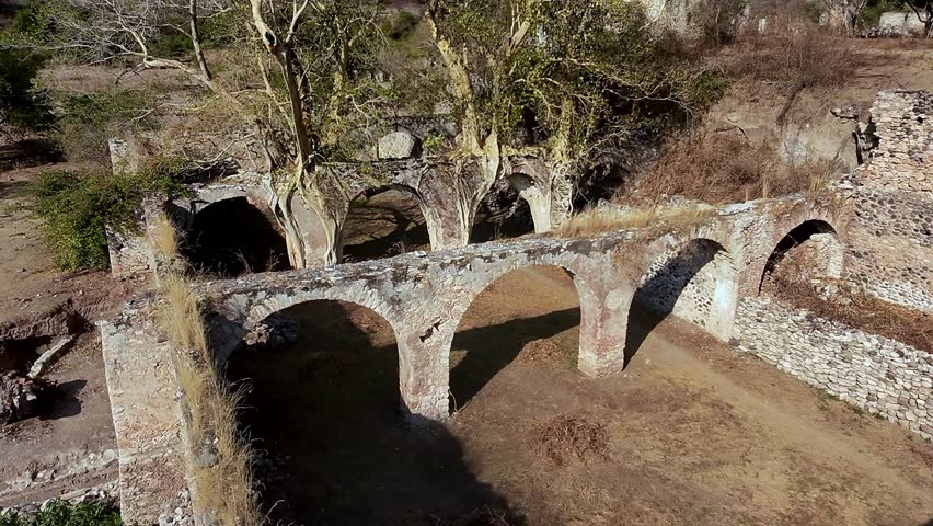 Aerial: Ex Hacienda de San Jacinto Ixtoluca, aqueducts with rocky wall during the day in La Mezquitera, Morelos, Mexico, crane down drone shot