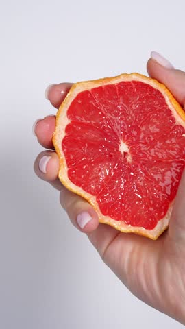 Hand squeezing juicy grapefruit wedge with fresh citrus splash on white background