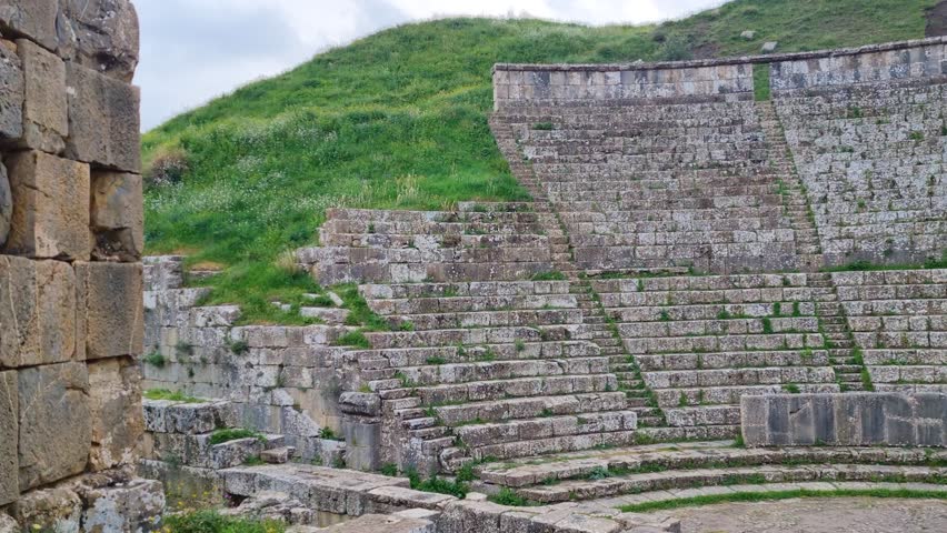 A view of the well-preserved small amphitheater in the ancient Roman city of Djemila, Algeria, captured on an overcast spring day