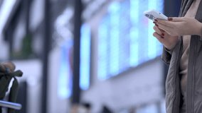 Woman is holding a cell phone in a busy airport. Concept of urgency and the need to stay connected while traveling - Powered by Shutterstock - Get 15% off with code: PIKWIZARD15