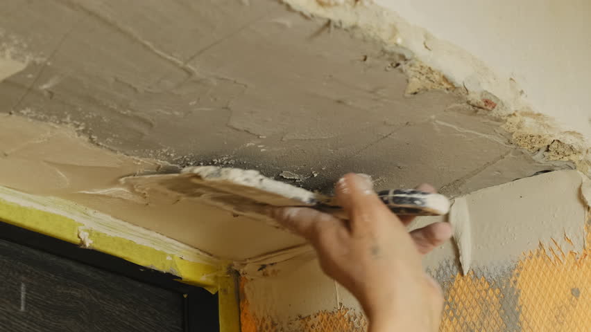 Skilled man plasterer applies putty on wall ensuring smoothness. Male technician covers gaps on plastered ceiling using trowel during renovation process
