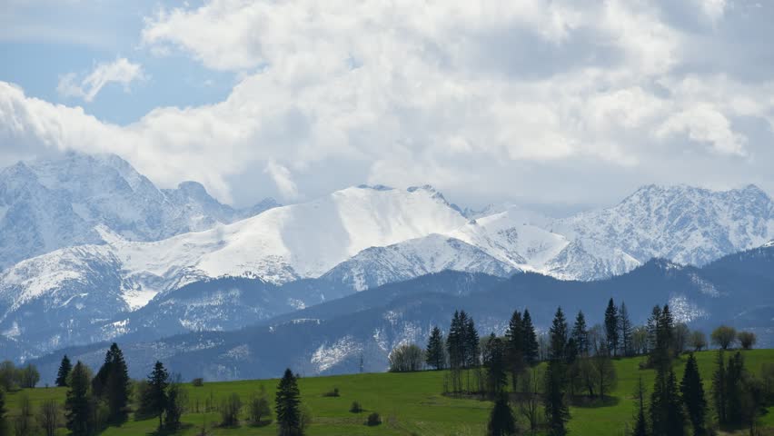White puffy clouds move quickly across the sky, with snow-capped mountain peaks in the background.