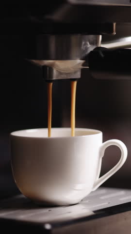 Vertical Video of Espresso machine making fresh coffee. Pouring coffee stream from machine in cup. Espresso in a white cup. Tasty coffee. Caffeine. Coffeeshop in the background with credit card NFC.