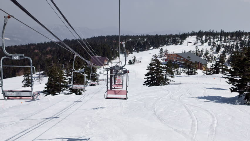 Ski lift POV on a bright sunny day with trees. Nagano, Japan