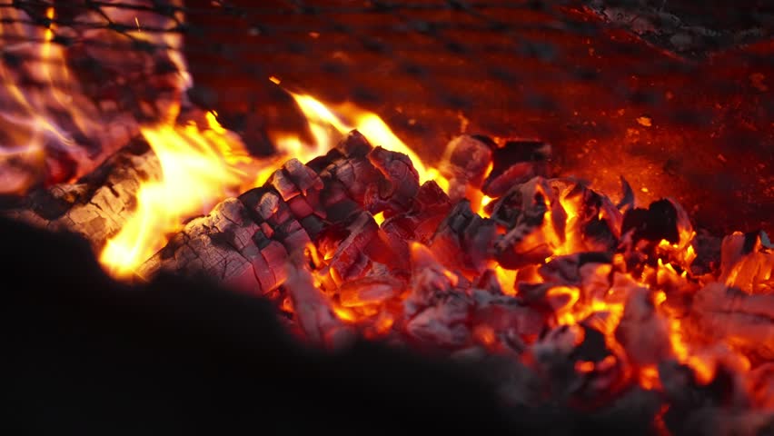 Close-up view of burning charcoal with bright orange flames and glowing embers in a barbecue grill