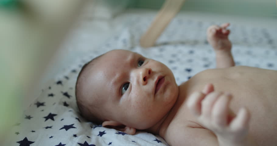 Newborn child with infant shuddering attacks lying on bed on his back looking. Close-up portrait.