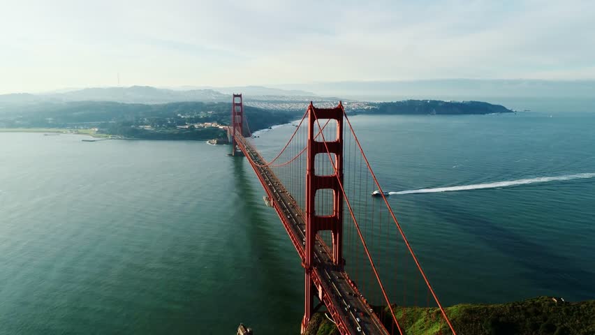 Golden Gate bridge and boat moving across still ocean under soft morning light