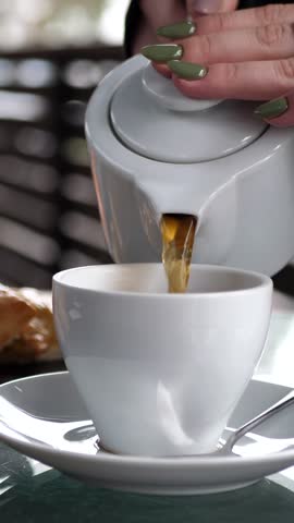 A woman's hand pours tea from a jug into a cup. Breakfast concept. Tea time