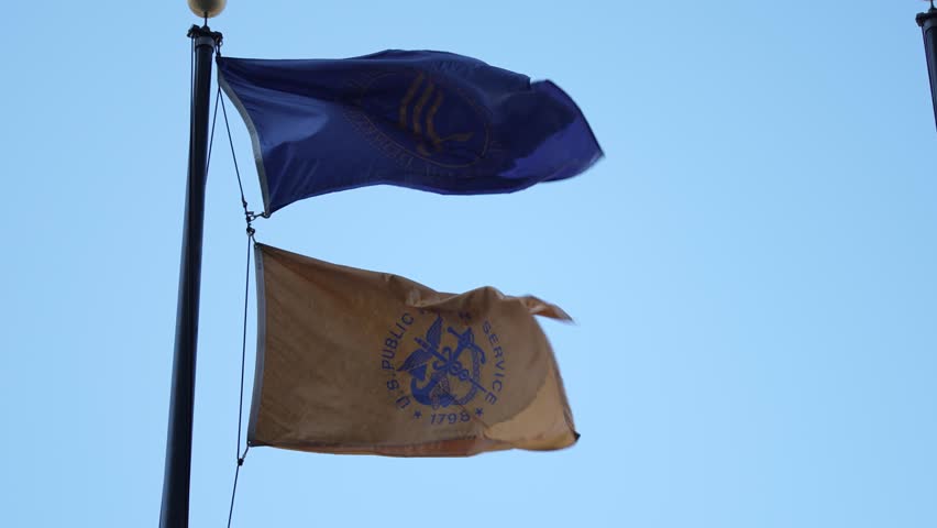Two flags are prominently displayed in front of the Health and Human Services building in Washington DC, showcasing federal symbols against a clear blue sky.