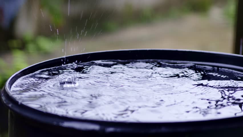 Rain drops filling up rainwater harvesting black barrel, slow motion