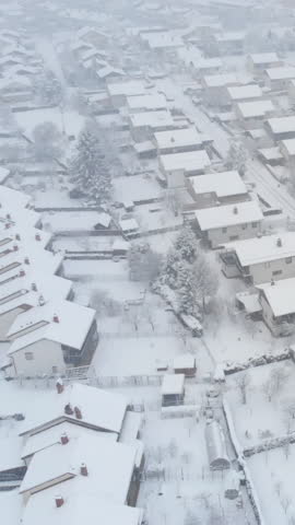 AERIAL: Pristine white snow covers the empty streets of an idyllic suburban neighborhood. Flying high above the rooftops of houses in the tranquil village on a snowy day. Blizzard in the suburbs.