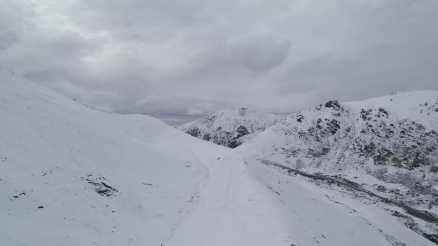 Aerial flyover snowy Hatchers Pass in Alaska during cloudy day. Famous hiking trail in America. Winter scene.