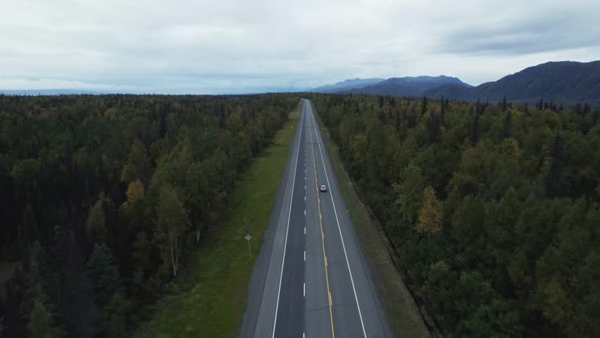 Driving on coutnryside road of Alaska forest, aerial drone follow view