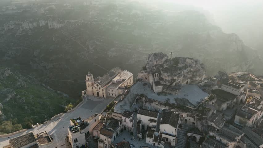 Aerial drone view of Basilica Cattedrale di Matera and the surrounding ancient stone dwellings in Matera, Italy. The historic landscape, carved into the rugged hills, highlights the city's medieval