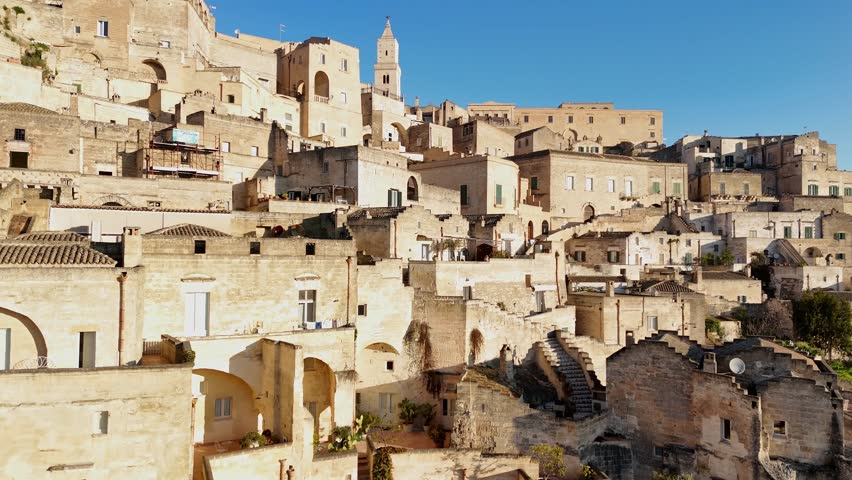 Aerial drone view of the Matera Cathedral bell tower rising above the ancient cityscape. The central part of the historic town showcases traditional stone dwellings and medieval architecture