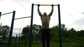 Muscular athlete doing pull ups on horizontal bar at sports ground. Young shirtless sportsman exercising at nature. Strong sporty man training outdoor. Concept of healthy and active lifestyle. Slow mo - Powered by Shutterstock - Get 15% off with code: PIKWIZARD15