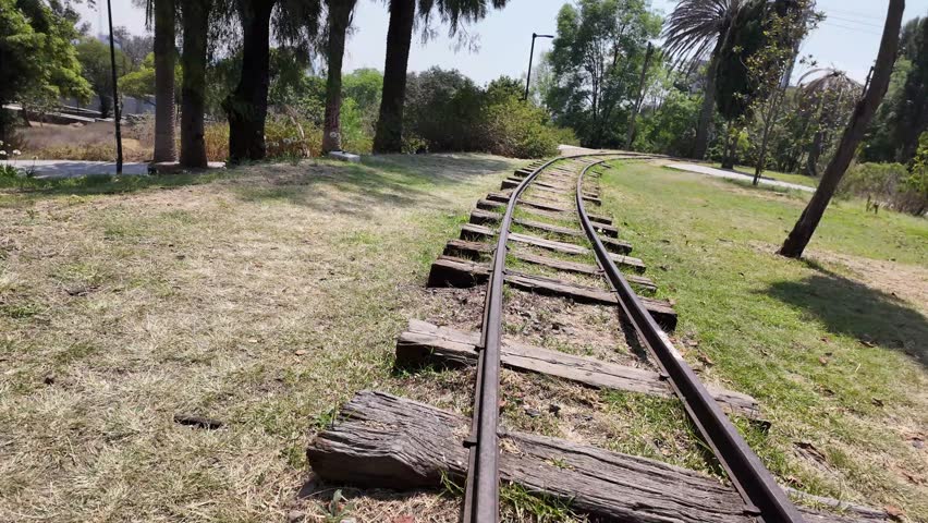 A train track with wooden boards on it. The track is in a park. There are trees in the background