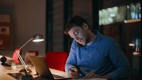 Overworked man talking smartphone read notebook at dark office under lamp light closeup. Stressed businessman calling massaging temples. Hardworking manager feeling headache from overtime laptop work. - Powered by Shutterstock - Get 15% off with code: PIKWIZARD15