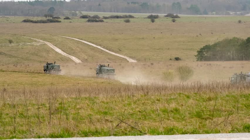 a convoy of British army MAN HX 8x8 logistic trucks carrying supplies across dusty countryside