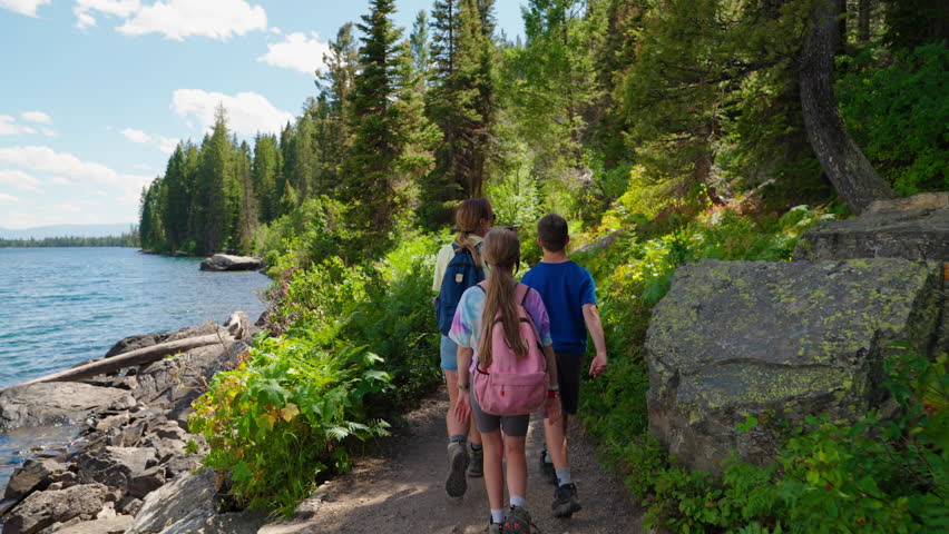 A family walks together along a scenic trail, exploring the outdoors, with lush forest surroundings and a tranquil lake enhancing the peaceful natural beauty.