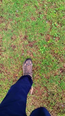 A first-person perspective video capturing the view of legs clad in athletic shoes, walking across a concerte sidewalk surface.