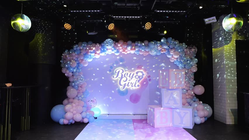 A large beautiful photo zone with pink and blue balloons and the inscription BOY OR GIRL at a gender party. Huge cubes with the inscription BABY. 