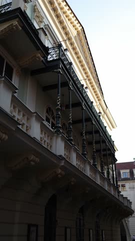 Vertical screen: Elegant historic building with detailed architectural elements and black-and-gold columns. The upward angle highlights the ornate balcony and classical design features.