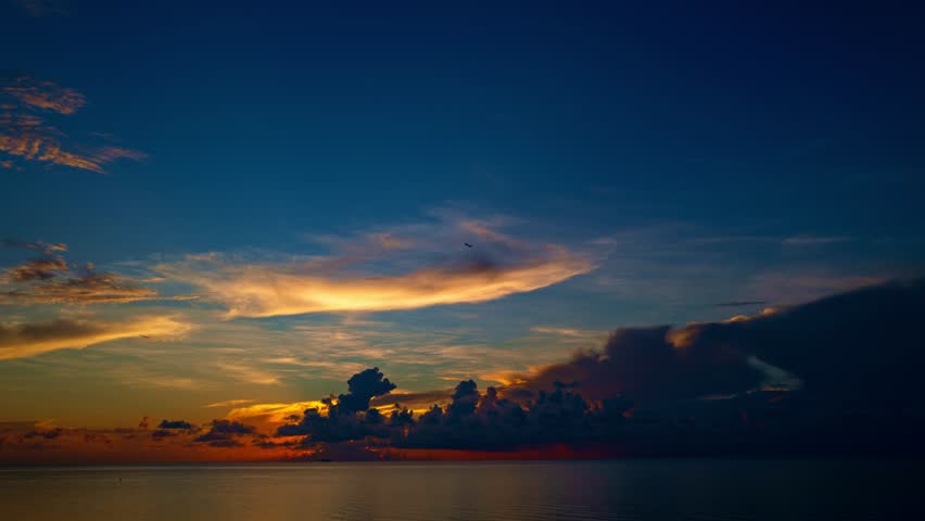 Sunset with sun and clouds on blue and orange dramatic sky with sun rays. Night Sky timelapse. Moving clouds at sunset. Evening Clouds. Dusk twilight sky time lapse. Dramatic epic evening sky.