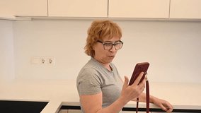 An elderly Caucasian woman talking on a video call on her smartphone in the kitchen.  - Powered by Shutterstock - Get 15% off with code: PIKWIZARD15