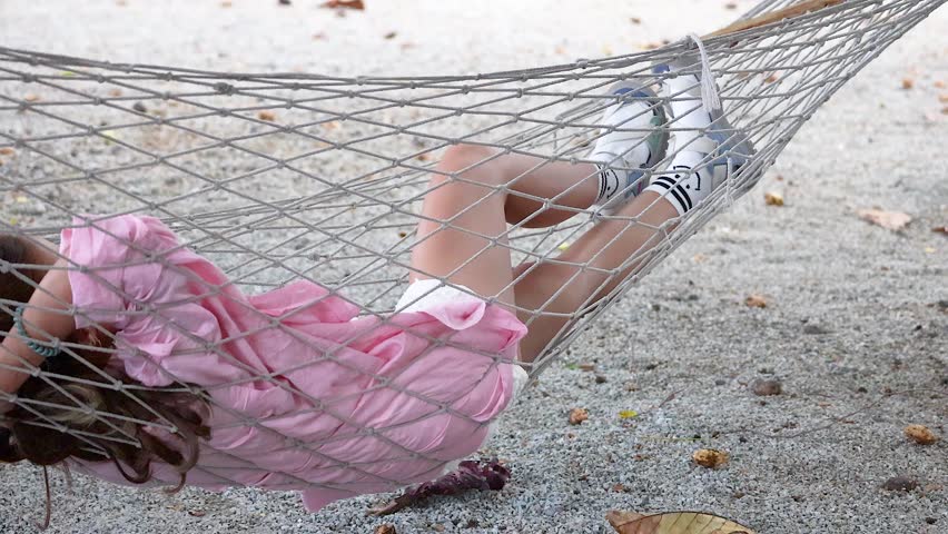 A woman in a pink dress relaxes on a hammock, gently swaying in a serene outdoor setting in Phuket
