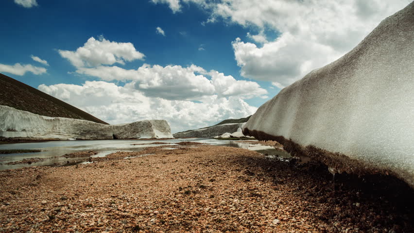 Glaciers on top of mountain time lapse video for background. Blocks of ice in rays of sunny day. Under blue sky with swirling clouds. Joyful peaceful cinematic wilderness. Concept of freedom calmness