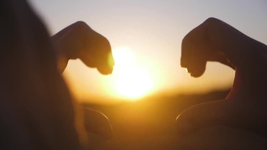 A young person forms a heart shape with hands against a sunset, symbolizing love, joy, and connection. A warm, emotional moment capturing peace, gratitude, and appreciation for life.