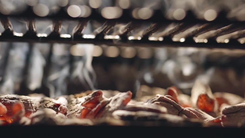 Slow motion along burning coals on grill. Fire glows under grate. Grill is great place to prepare delicious delights. Classic barbecue with burning coals. Hot coal is ready for cooking, copy space AD