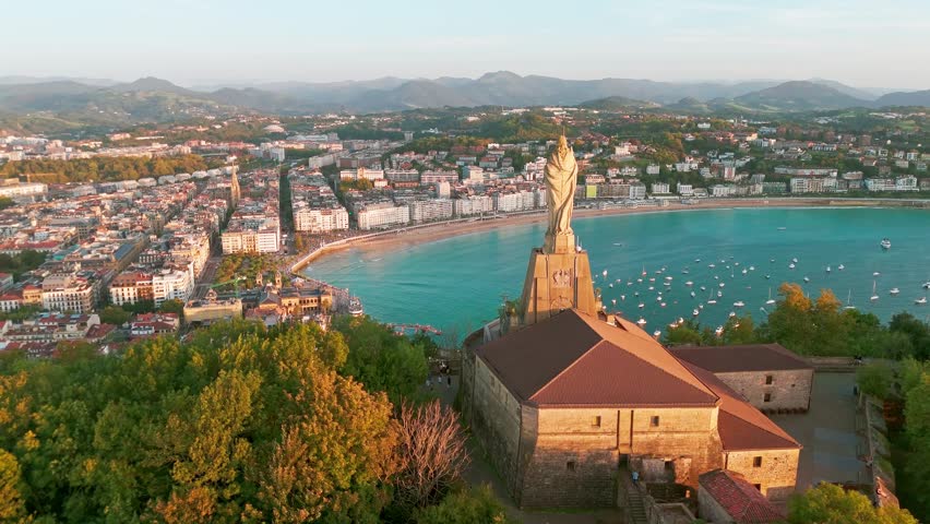 Aerial view of the beautiful coast of San Sebastian at sunset, Basque country, Spain. Flying over the statue of Christ stands watch over magnificent Bay of Biscay, Donostia. Orbit shot