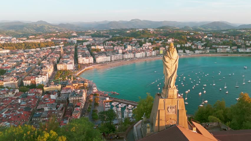 Aerial view of the beautiful coast of San Sebastian at sunset, Basque country, Spain. Flying over the statue of Christ stands watch over magnificent Bay of Biscay, Donostia. Orbit shot