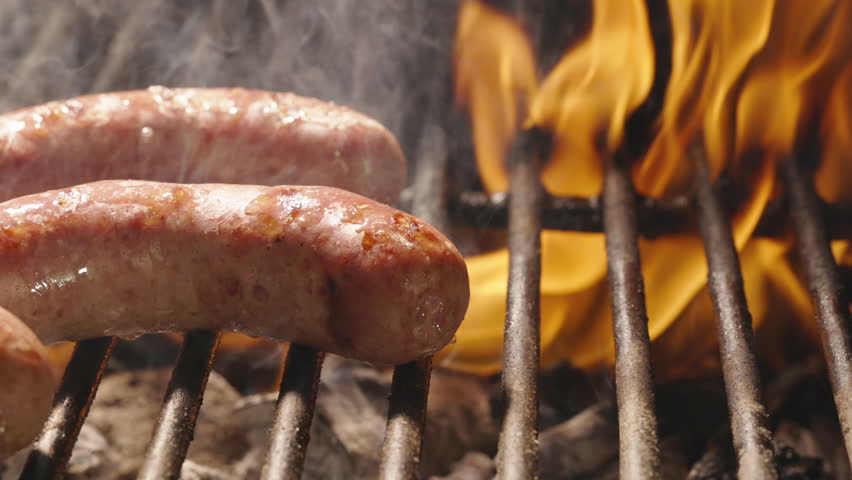 Close-up.Flame dances beautifully across grill grate, bringing sausages to readiness, hot grill, sizzling sausages. Heat of flame browns the sausages, releasing delicious juice from them. Cinematic AD
