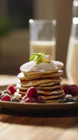 Side view of pancakes adorned with juicy berries, syrup, and sugar powder, kitchen. Leisurely cozy morning, essence of lifestyle, food, cooking, and domestic life. Vertical video, no people, cinematic