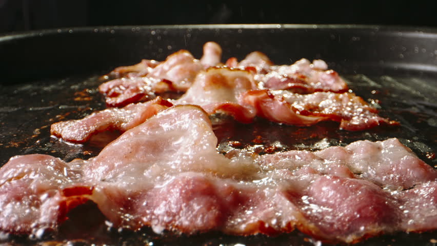 Frying halal beef bacon in pan side view close up slow motion. Bacon can be enjoyed in moderation as part of balanced diet. Sizzling pan-fried bacon slices tempt with their enticing aroma flavors