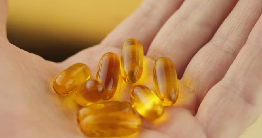 Golden vitamin capsules on palm. Dietary supplements and nutrition concept. Health care and wellness products. Macro photography of pills for immunity boost. Medicine and pharmaceutical drugs