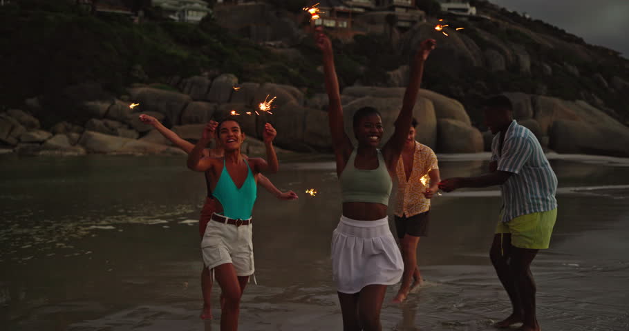 Happy, friends and dancing with sparkler on beach for ocean party, travel reunion and bonding together. Group, people and fireworks with rhythm movement, holiday celebration and nightlife for getaway