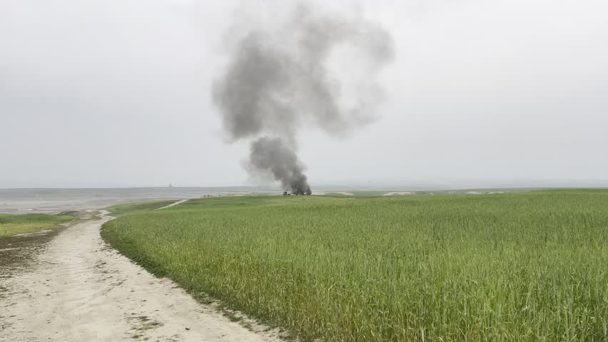black smoke rising in sky due to fire in green fields
