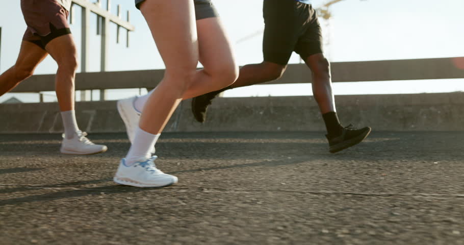 Fitness, legs and group with running on bridge for marathon training, cardio exercise and performance pace. People, runner club and sneakers in road for wellness competition, morning jog and workout