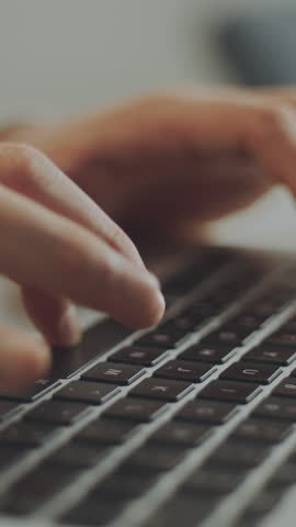 Close-up shot of hands of a bearded handsome man sitting at table and typing on laptop while working remotely from home