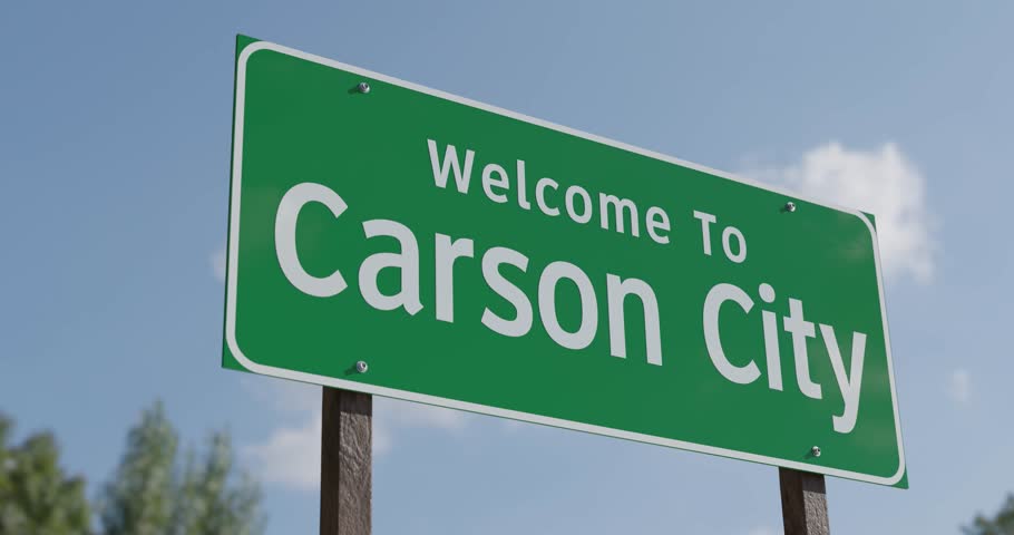Driving By A Welcome To Carson City, Nevada Green Road Sign Against a Blue Sky and Clouds - United States Capital Series.