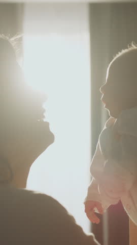 Happy young mother lifting up her newborn baby in slow-motion at home while she is smiling